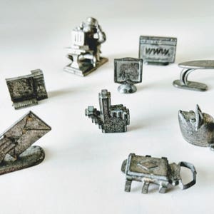 May include: A selection of small, silver-coloured metal figurines, including a computer, mouse, desk, and a person at a computer. Other figurines include a computer monitor, a website, a mouse cursor, a mouse, a mailbox, and a lock.