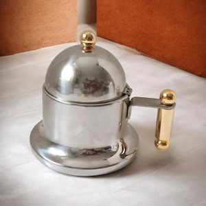 May include: A stainless steel coffee maker with a domed lid and a gold-coloured handle. The handle and lid knob have a gold finish. The coffee maker has a classic design, likely for brewing espresso or stovetop coffee.