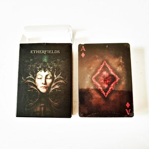 May include: A deck of playing cards with a dark, artistic design. The card box features the text "ETHERFIELDS" and an illustration of a woman's face. The Ace of Diamonds card is visible, with a red diamond design.