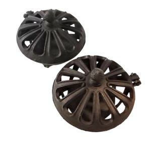 May include: Two dark bronze bottle stoppers. Each stopper features a round, openwork design with a central knob and a small decorative element. The metal stoppers have a vintage aesthetic. The design is reminiscent of a wheel.