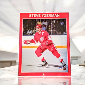 May include: A hockey card with a red border, featuring Steve Yzerman in a Detroit Red Wings uniform. The image shows the player skating on the ice. The text "STEVE YZERMAN" is displayed at the top of the card.