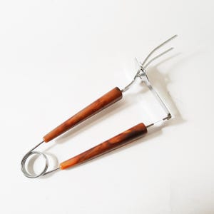May include: A pair of silver tongs with brown wooden handles. The tongs have a spring mechanism and a three-pronged end.