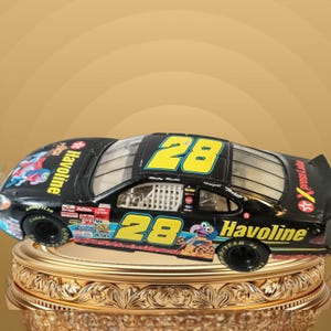 May include: A black die-cast stock car model featuring the number 28 in yellow on the roof and sides. The car displays Havoline branding, various sponsor logos, and a graphic of the Muppet character Gonzo on the bonnet and side panels.