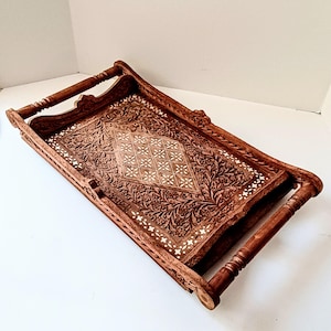 May include: A rectangular wooden serving tray with detailed floral carvings and a diamond-shaped inlaid design. The tray has two handles and measures approximately 46 cm long and 30 cm wide.