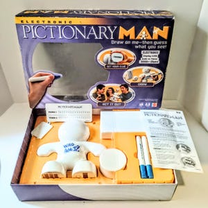 May include: Electronic Pictionary Man board game set in a cardboard box. Includes a white plastic figure with the text WHO AM I? written on the chest, two blue markers, a white circular base, a white rectangular component, and an instruction manual.
