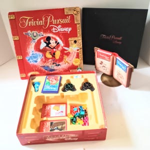 May include: A red Trivial Pursuit Disney Edition board game box featuring Mickey Mouse and other Disney characters. The game includes cards, game pieces, and a black box with the game title.