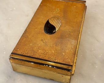 Peut inclure: Une boîte rectangulaire de couleur dorée avec un motif ovale noir et or sur le dessus. La boîte a une surface texturée et une bordure noire autour des bords.