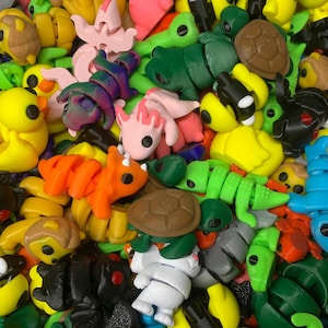 May include: A collection of colourful 3D printed figurines, including a pink dragon, a green turtle, a yellow duck, and an orange dinosaur. The figurines are made of plastic and have a variety of textures and details.