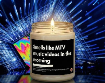 Op de afbeelding: Een brandende sojakaars in een glazen pot. Het zwarte etiket luidt "Smells like MTV music videos in the morning." De kaars is 255 g. De achtergrond is een blauw en paars abstract ontwerp.