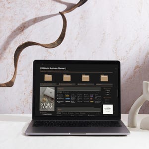 May include: A laptop displaying a business planner interface with the text "Ultimate Business Planner." The screen shows organized folders and project sections. The words "Start Today" are visible on a small image. The laptop is on a white surface.