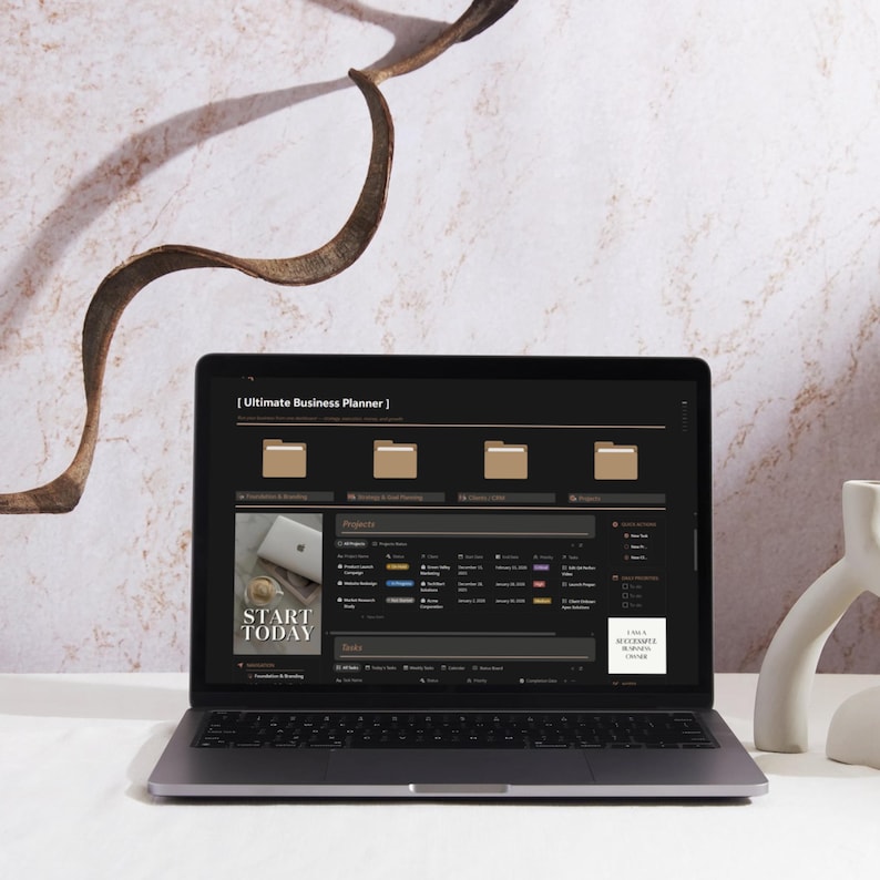 May include: A laptop displaying a business planner interface with the text "Ultimate Business Planner." The screen shows organized folders and project sections. The words "Start Today" are visible on a small image. The laptop is on a white surface.