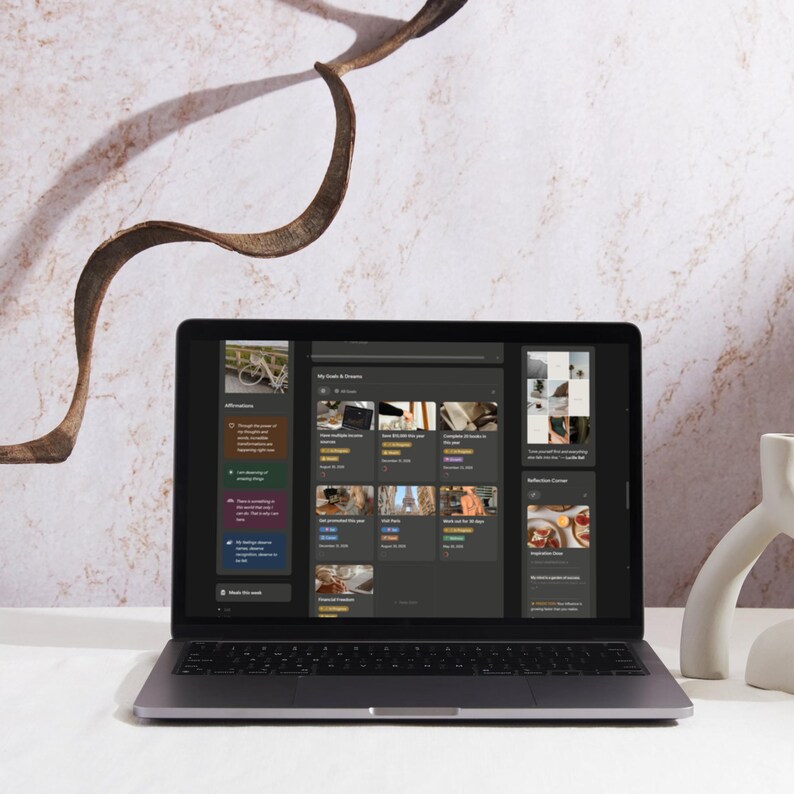May include: A silver laptop displaying a digital interface with various icons and text. The screen shows a dark-themed application with multiple image thumbnails and text. A white ceramic decorative object is on the right. The background features a marble wall and a curved brown branch.
