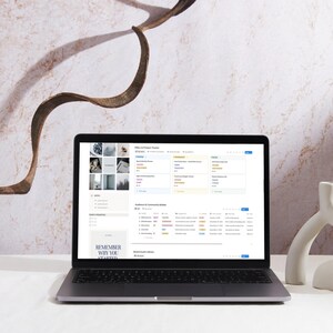 May include: A silver laptop displaying a webpage with data tables and a menu. The screen shows a list of items with various categories. The text "REMEMBER WHY YOU STARTED" is visible on the screen. A white decorative object is on the right.