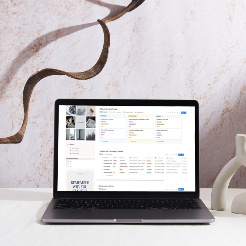 May include: A silver laptop displaying a webpage with data tables and a menu. The screen shows a list of items with various categories. The text "REMEMBER WHY YOU STARTED" is visible on the screen. A white decorative object is on the right.
