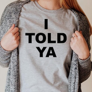 May include: A gray t-shirt with the text "I TOLD YA" printed in black.