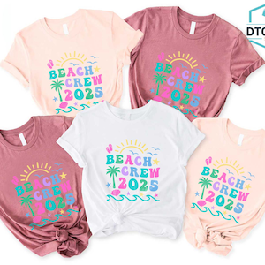 Puede incluir: Cinco camisetas en varios colores, incluyendo blanco, rosa y malva. Cada camiseta presenta el texto "BEACH CREW 2025" en un dise&ntilde;o colorido con un sol, una palmera y olas. Las camisetas son de manga corta.