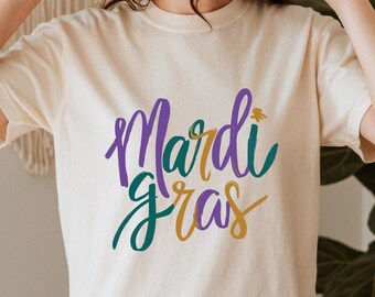 Camiseta Comfort Colors® con el logo de Mardi Gras, color morado, verde y dorado, ideal para fiestas en Nueva Orleans.