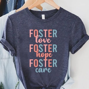 May include: A navy blue t-shirt with the text "FOSTER love FOSTER hope FOSTER care" in pink and blue lettering.