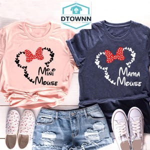K&ouml;nnte beinhalten: Zwei T-Shirts, eines in Rosa und eines in Marineblau, mit einer wei&szlig;en Umrandung von Mickey Mouse Ohren und einer roten Schleife. Das rosa T-Shirt sagt "Mini Mouse" und das marineblaue T-Shirt sagt "Mama Mouse".