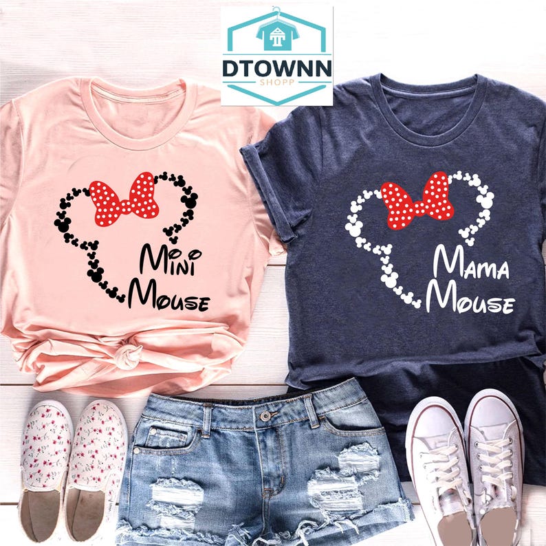 K&ouml;nnte beinhalten: Zwei T-Shirts, eines in Rosa und eines in Marineblau, mit einer wei&szlig;en Umrandung von Mickey Mouse Ohren und einer roten Schleife. Das rosa T-Shirt sagt "Mini Mouse" und das marineblaue T-Shirt sagt "Mama Mouse".