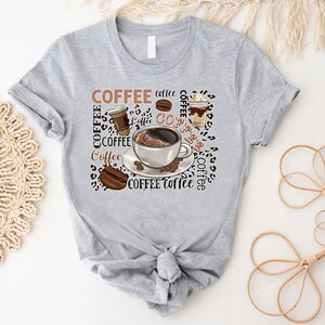 May include: Grey t-shirt with a coffee themed design. The design features a cup of coffee, coffee beans, and the word "COFFEE" repeated multiple times.