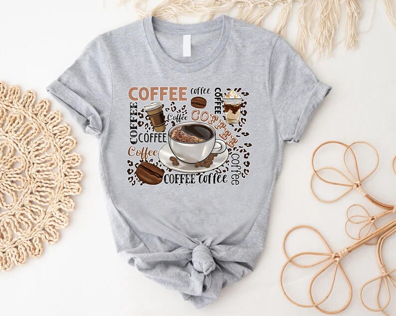 May include: Grey t-shirt with a coffee themed design. The design features a cup of coffee, coffee beans, and the word "COFFEE" repeated multiple times.