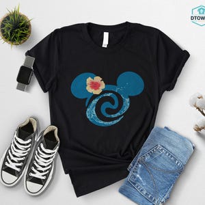 May include: Black t-shirt featuring a blue Mickey Mouse head design with a flower and wave pattern. The shirt is paired with blue jeans, black sneakers, and a smartwatch. A small potted plant is also visible.