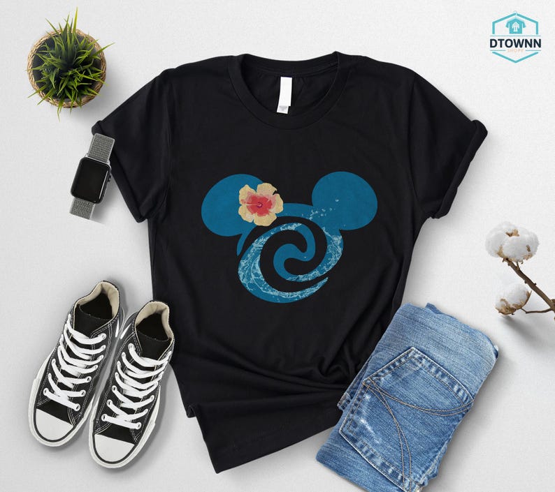 May include: Black t-shirt featuring a blue Mickey Mouse head design with a flower and wave pattern. The shirt is paired with blue jeans, black sneakers, and a smartwatch. A small potted plant is also visible.
