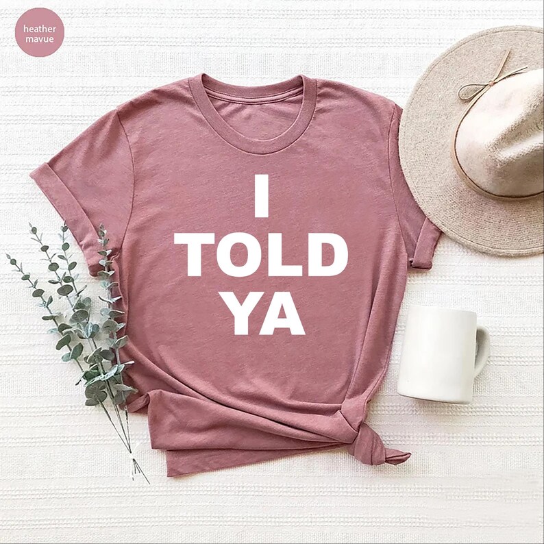 May include: A heather mauve t-shirt with the text "I TOLD YA" printed in white.
