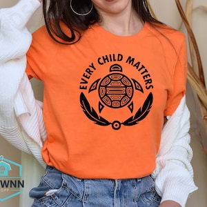 May include: Orange t-shirt with a black graphic of a turtle with the text "Every Child Matters" around it.