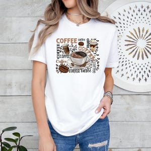May include: White t-shirt with a brown and white graphic design featuring a coffee cup, coffee beans, and the word "COFFEE" repeated multiple times.