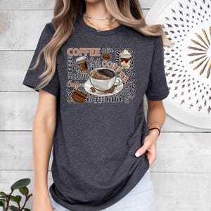 May include: A dark grey t-shirt featuring a graphic design of coffee cups, coffee beans, and the word "coffee" repeated in various fonts and sizes.