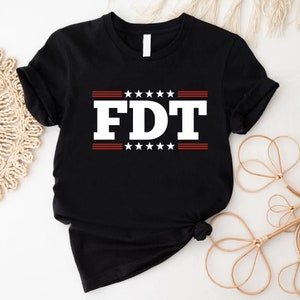 May include: Black t-shirt with white text that says "FDT" in bold letters. The text is surrounded by red stripes and white stars.