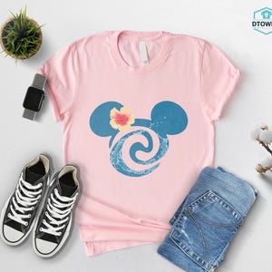 May include: A light pink t-shirt featuring a blue Mickey Mouse silhouette with a floral design. The shirt is paired with black sneakers, blue jeans, and a smartwatch. A small potted plant and cotton sprig are also visible.