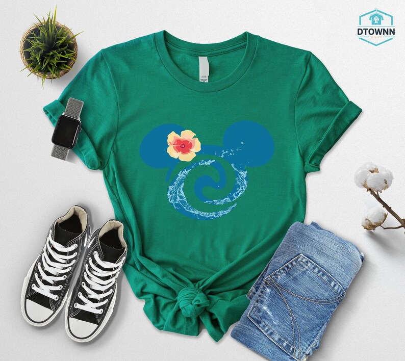May include: A green t-shirt featuring a blue Mickey Mouse silhouette with a yellow and red flower and a water design. The shirt is paired with blue jeans and black sneakers with white laces.