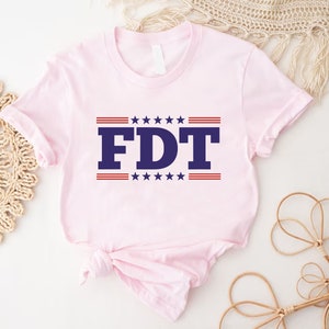 May include: Pink t-shirt with a blue and red graphic that says "FDT" with stars and stripes.