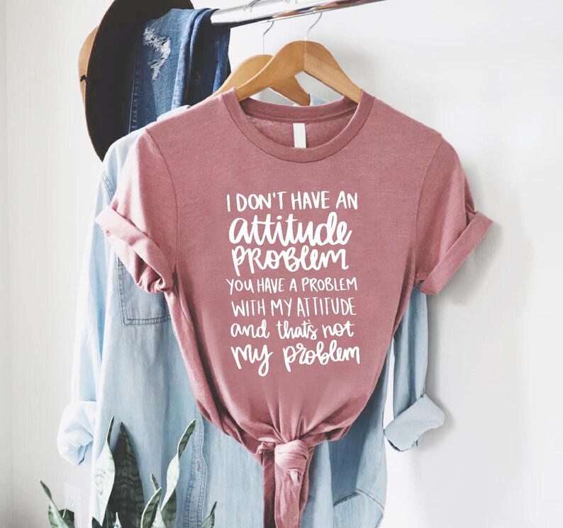 K&ouml;nnte beinhalten: Staubrosafarbenes T-Shirt mit wei&szlig;em Text: "I DON'T HAVE AN attitude PROBLEM YOU HAVE A PROBLEM WITH MY ATTITUDE and that's not my problem". Das T-Shirt ist unten geknotet.