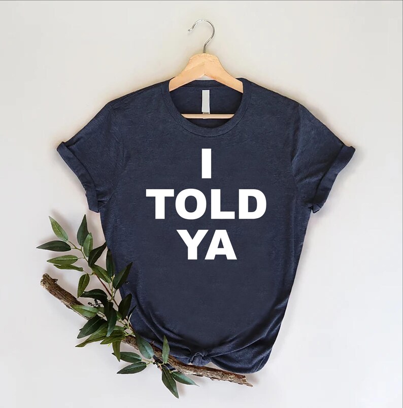 May include: A dark blue t-shirt with the text "I TOLD YA" printed in white.