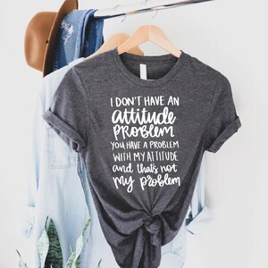 K&ouml;nnte beinhalten: Dunkelgraues T-Shirt mit dem wei&szlig;en Text "I don't have an attitude problem, you have a problem with my attitude and that's not my problem". Das Shirt ist unten geknotet.