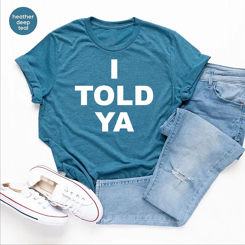 May include: A teal blue t-shirt with the text "I TOLD YA" printed in white.