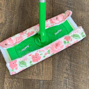 May include: A green Swiffer mop head with a white and pink floral fabric cover. The cover has a white border and pink flowers with green leaves.