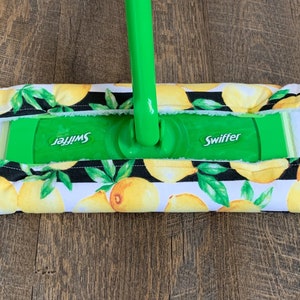 May include: A green Swiffer mop with a lemon print cover. The cover has black stripes and yellow lemons with green leaves.