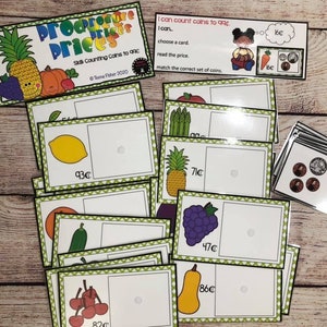 May include: A set of colorful produce price cards with matching coin sets. The cards feature images of fruits and vegetables like pineapple, grapes, lemons, cherries, and pumpkins. The cards have a green border and a white background with the price written in cents. The coin sets are in a stack and feature US coins.