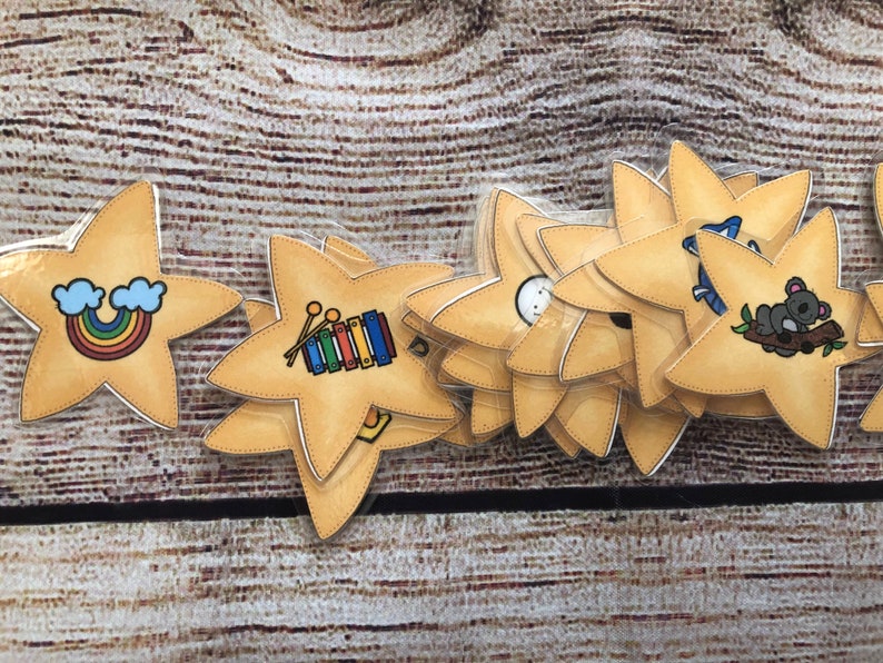 Puede incluir: Conjunto de tarjetas did&aacute;cticas en forma de estrella con ilustraciones coloridas. Incluyen un arco&iacute;ris, un xil&oacute;fono y un koala. Las tarjetas est&aacute;n sobre una superficie de madera.