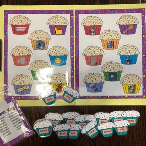 May include: A colorful educational game for kids featuring cupcakes with different pictures inside. The game includes a set of cupcake-shaped pieces with words on them, such as "house", "drum", "sun", and "ship".
