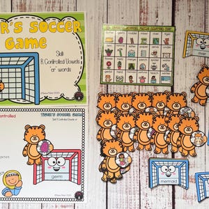 May include: An educational game set titled Tiger's Soccer Game featuring R-controlled vowels. Includes two instructional sheets, a grid answer key, and multiple cut-out pieces depicting orange tigers with soccer balls and blue or red soccer goals.