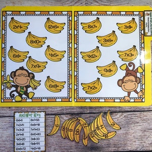 May include: A yellow and white printable folder with a monkey theme. The folder has multiplication problems with bananas and monkeys. The answer key is on the bottom of the folder. The folder is on a wooden surface.