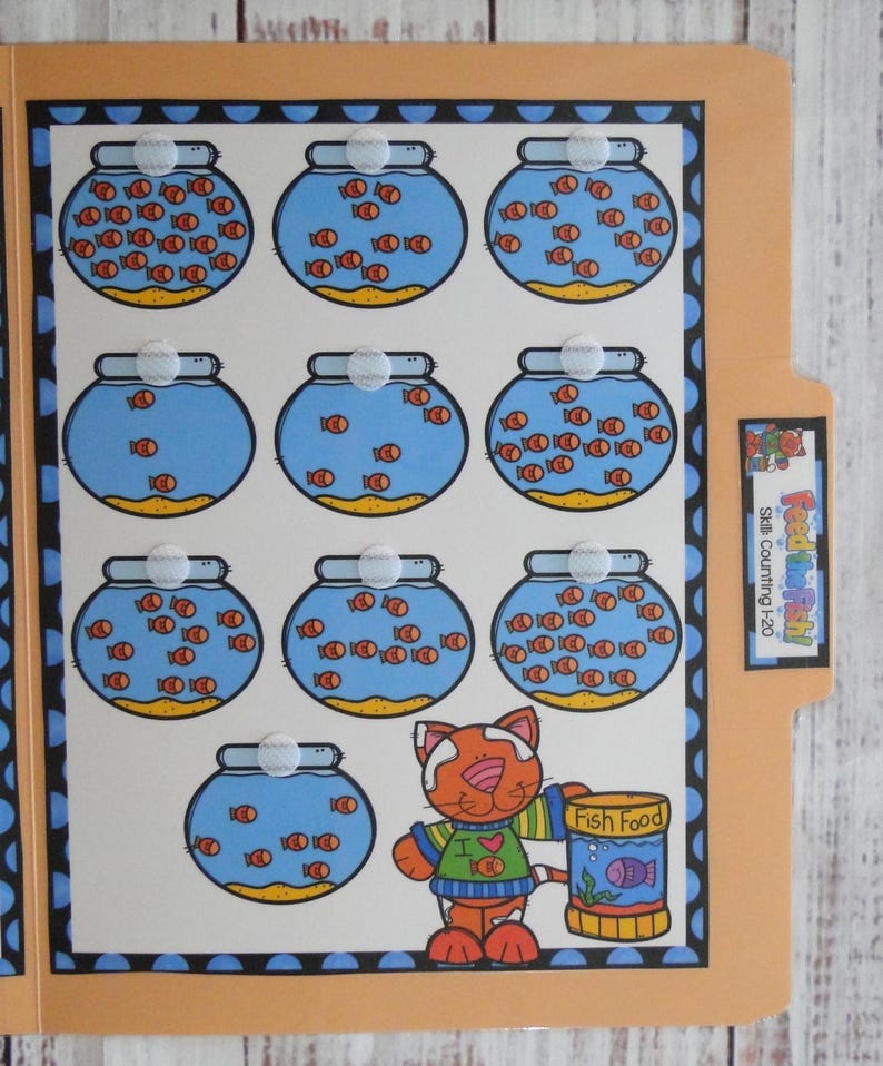 May include: A tan file folder educational activity titled Feed the Fish! Skills Counting 1-20. The interior features ten illustrations of blue fishbowls with orange fish and a cartoon cat holding a yellow container labelled Fish Food.
