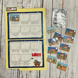 Könnte beinhalten: Ein gelbes und blaues illustriertes Brettspiel für Kinder über die Geburt Jesu. Das Spiel enthält 11 nummerierte Felder mit Bildern und Text, die die Geschichte der Geburt Jesu beschreiben. Das Spiel enthält auch 11 kleine Karten mit Bildern, die zu den Feldern auf dem Brett passen.