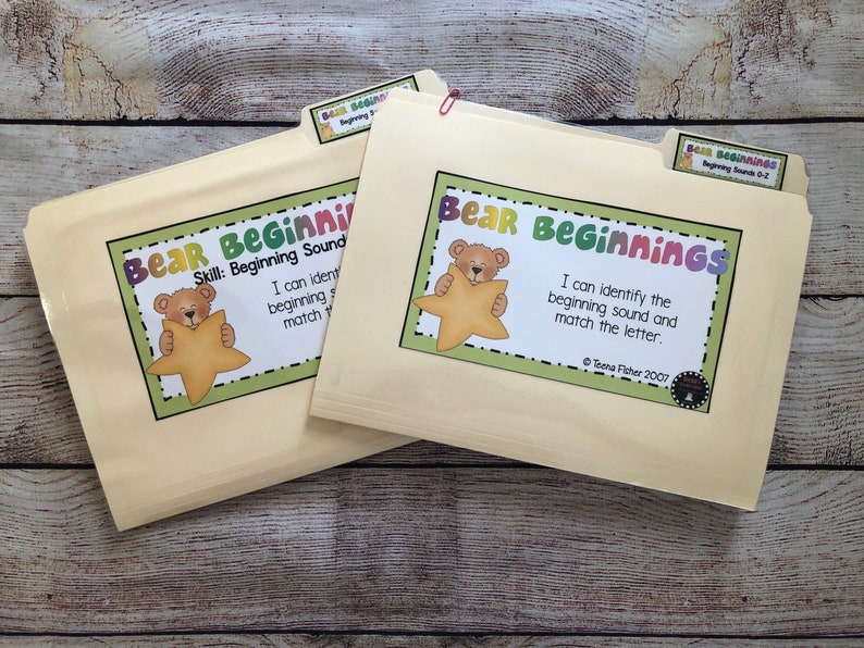 Puede incluir: Dos carpetas beige con etiquetas que dicen "Bear Beginnings". Cada etiqueta presenta un oso de dibujos animados sosteniendo una estrella. El texto en las etiquetas dice "Puedo identificar el sonido inicial y hacer coincidir la letra".